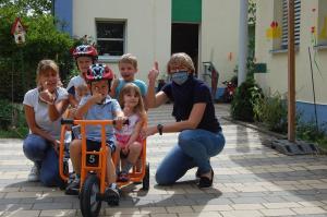 Erzeiherin Kinder und Radverkehrsbeauftragte auf und um das neue Kinderfahrzeug versammelt, Kita Abenteuerland