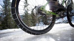 Fahrrad auf Schneebedecker Fahrbahn von unten HInterrad mit Schneeketten Schnee
