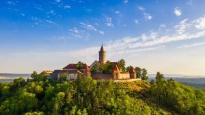 Blick auf die Leuchtenburg in der Mitte des Bildes die Burg mit allen Teilgebäuden und dem Burgfried. Gelegen auf einem bewaldteten Hügel im Hintergrund blauer Himmel mit einigen Wolken, Spätsommmer