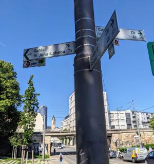 Im Vordergrund ein Fahrradwegweiser im Hintergrund Bick von Osten von der Camsdorfer Brücke in Richtung Innenstadt Jena