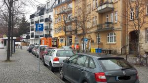 Stadtstraße mit parkenden Autos im Vordergrund, gepflasterter Gehweg, Bäume ohne Laub