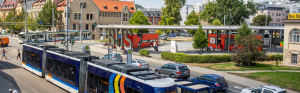Im Vordergrund eine Straßenbahm im Hinergrund rechts Autos auf der Weigelstraße und der Busbahnhof, im Hintergrund oberhalb der Straßenbahn das Volkshaus Jena