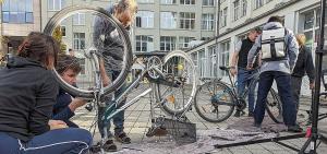 Fahrräder stehen umgedreht mit den Rädern nach oben zum Reparieren  da, mehrere Personen reparieren diese