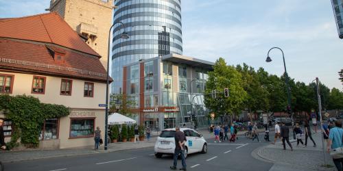 Blick auf den befahrenen und von Fußgängern belaufenen Löbdergraben mit Johannistor und JenTower im Hintergrund