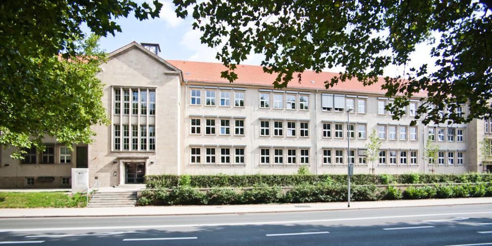 Dienstgebäude Anger 26 - Haupteingang, im Vordergrund Bäume und Straße, blauer Himmel