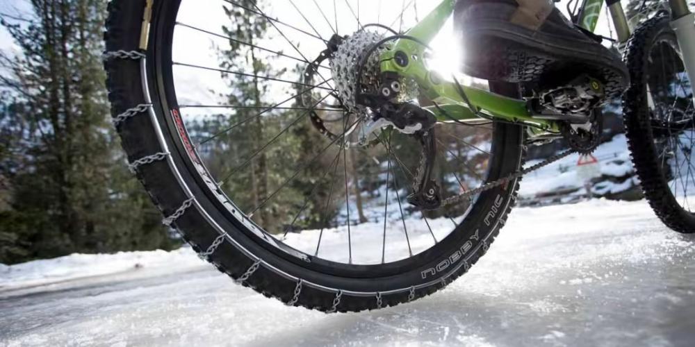 Fahrrad auf Schneebedecker Fahrbahn von unten HInterrad mit Schneeketten Schnee