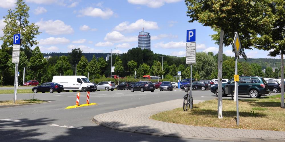 Blick auf den Seidelparkplatz in Jena im Vordergrunddie EInmündung, Bäume einzenlne Fahrzeuge, im Hintergrund ist der Uniturm zu sehen.