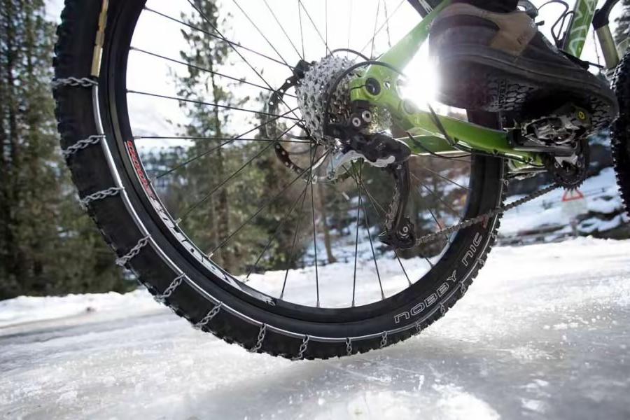 Fahrrad auf Schneebedecker Fahrbahn von unten HInterrad mit Schneeketten Schnee